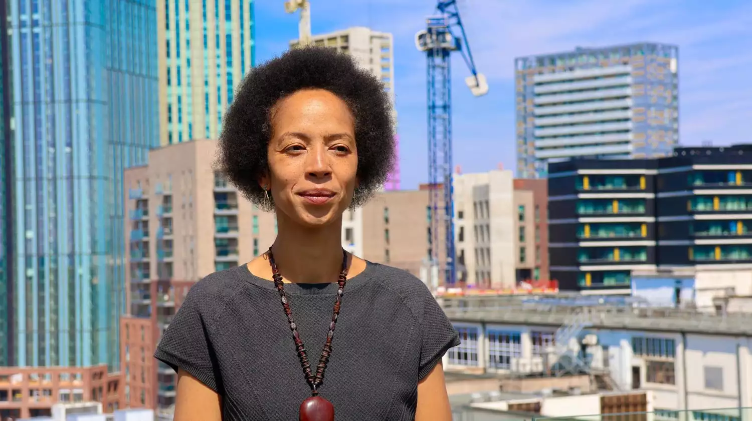 A person stood on a building, with Manchester's skyline and cranes behind them on a sunny day