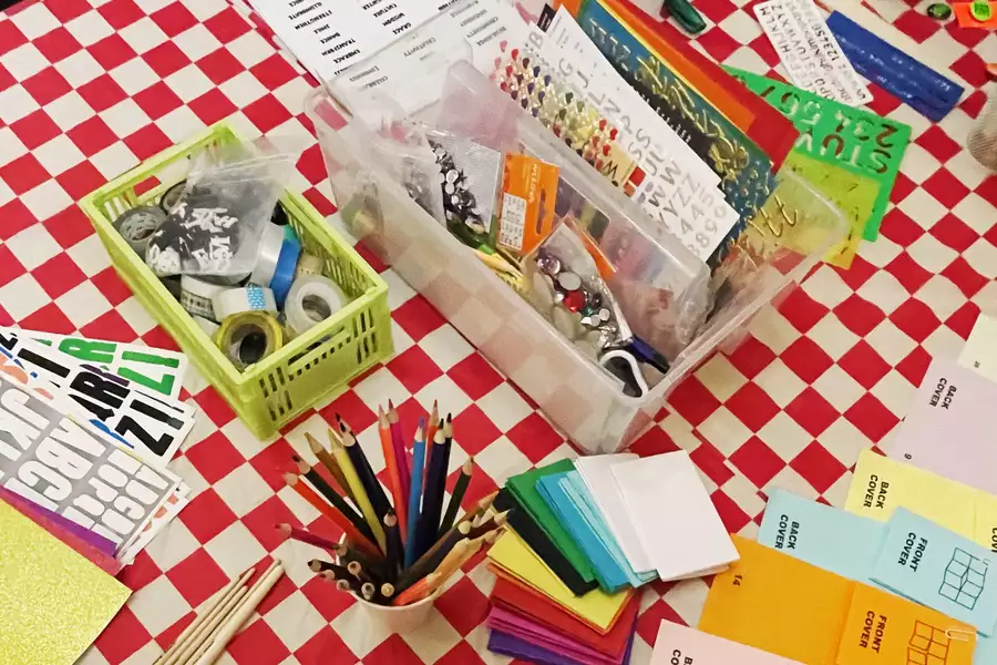 A craft table with red and white chequered table cloth, pencils and crafts