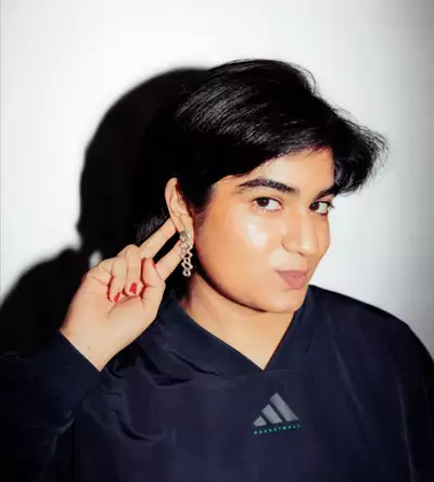 Areesha Ali wearing a black Adidas sweatshirt and silver earrings on a white background