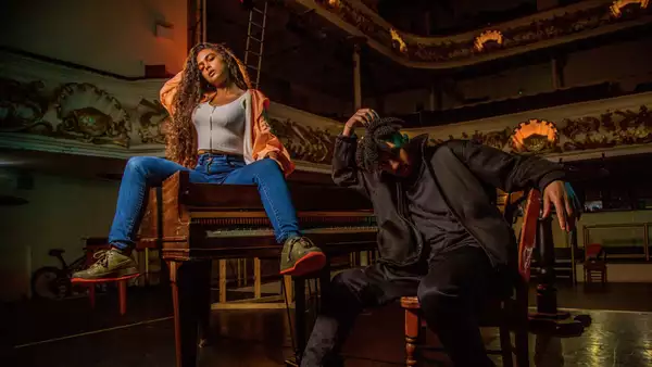 A photo of two people posing next to a grand piano in a concert hall