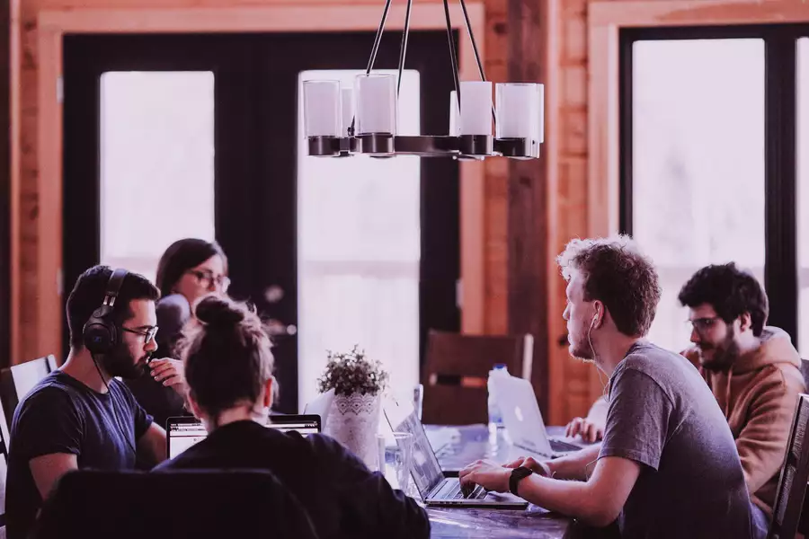 A group of people are sat around a table looking at their laptops in a working space.