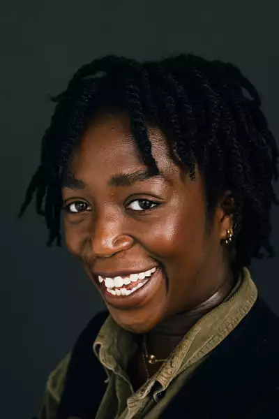 Headshot of Mayowa Ogunaike smiling on a dark grey background