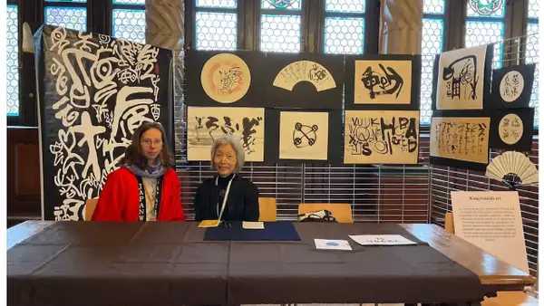 Two people sat behind a table displaying their artwork and calligraphy