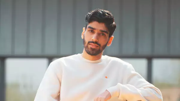 Hindh stood outside wearing a grey sweatshirt. The background is blurred.