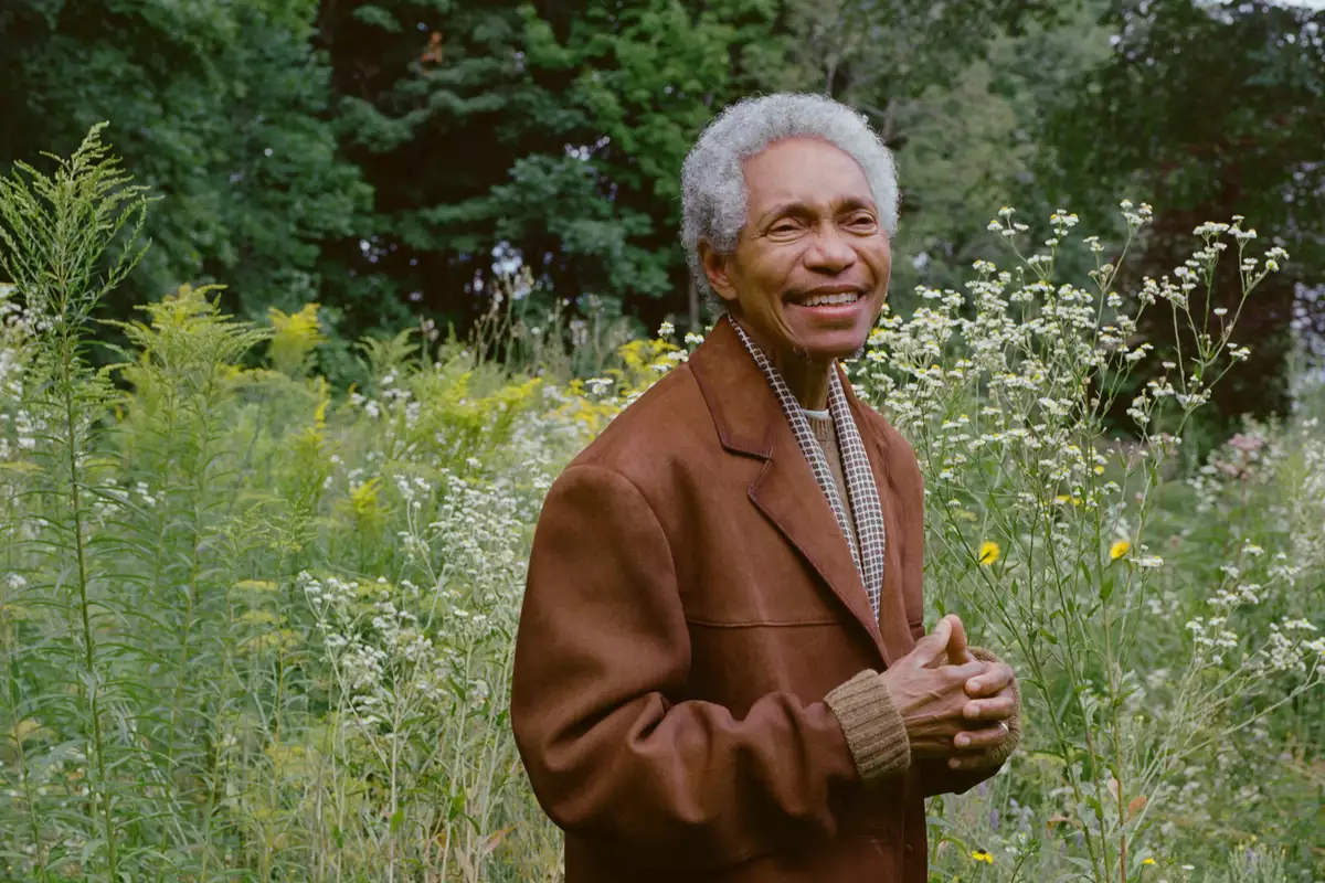 Glenn wearing a brown jacket and smiling, stood outside in a field of flowers