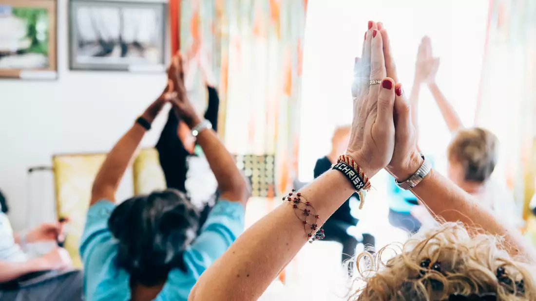 4 people taking part in a yoga class with their hands above their heads in a prayer position