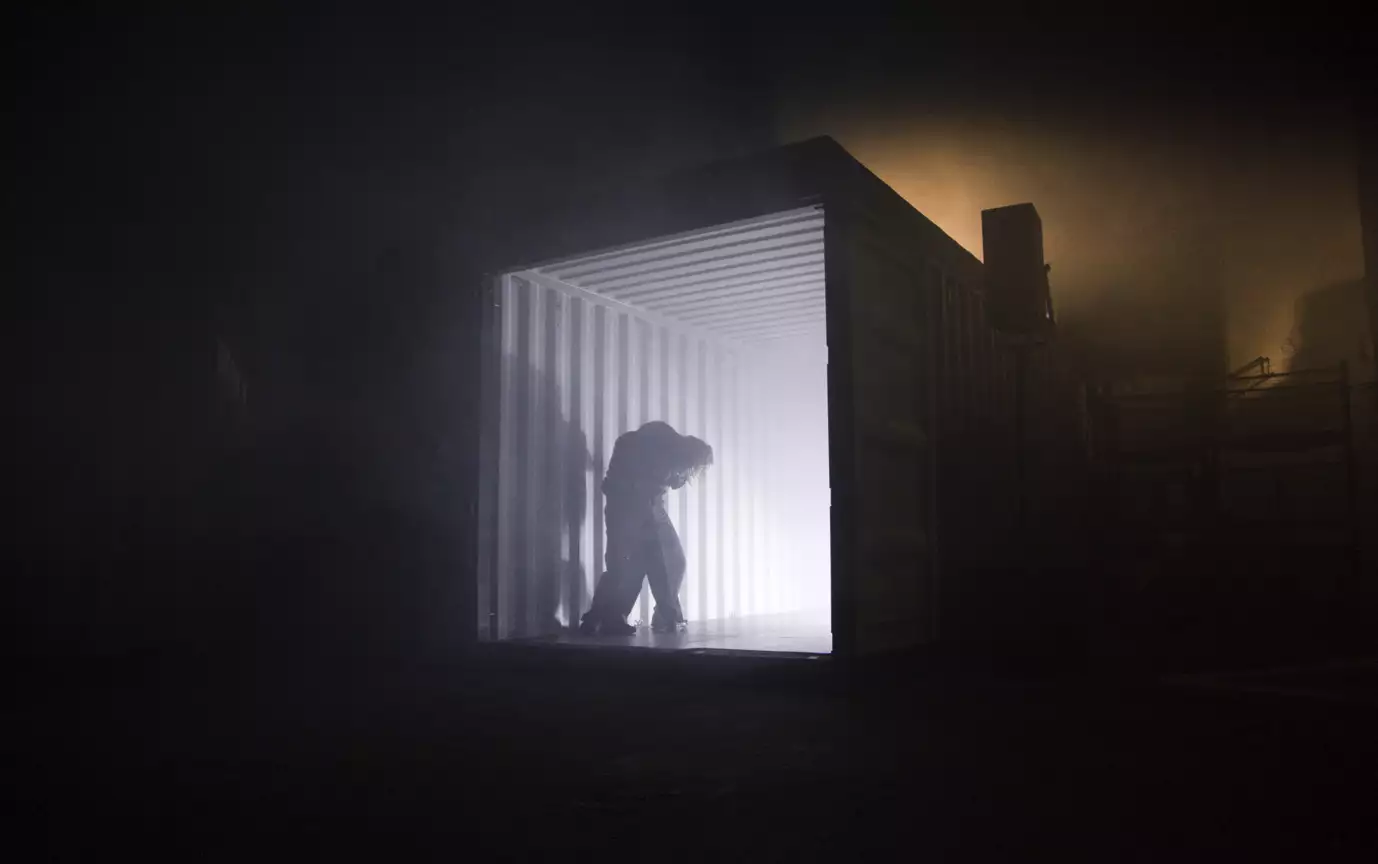 A photo of a dark warehouse space and a person stood silhouetted against a bright light coming from a shipping container