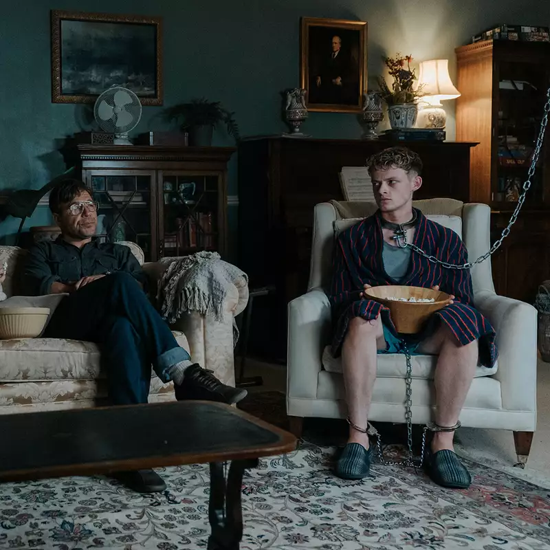 Still from The Good Boy showing a family sat on a sofa in a living room, with one man in chains