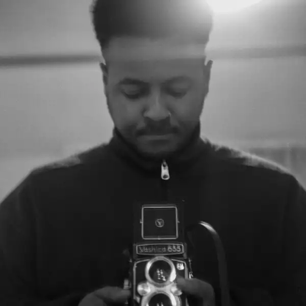 Black and white headshot of Nico Walker looking down at a camera