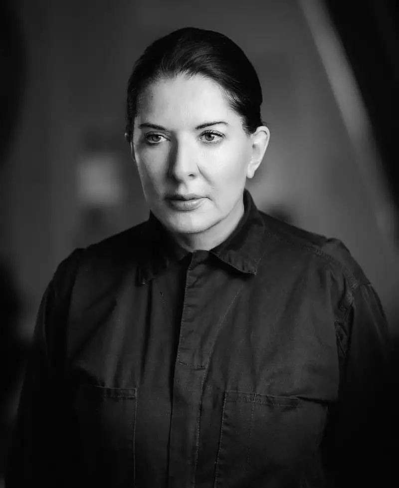 Black and white photo of Marina Abramovic with her hair pulled back, wearing a black jumper