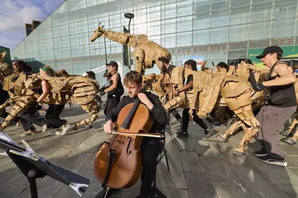 A photo of animal puppets outside the football museum with a cellist from Manchester Camerata orchestra