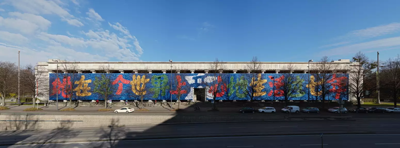Ai Weiwei's artwork 'Remembering' on the side of the Haus der Kunst on a sunny day. Cars are driving past it.