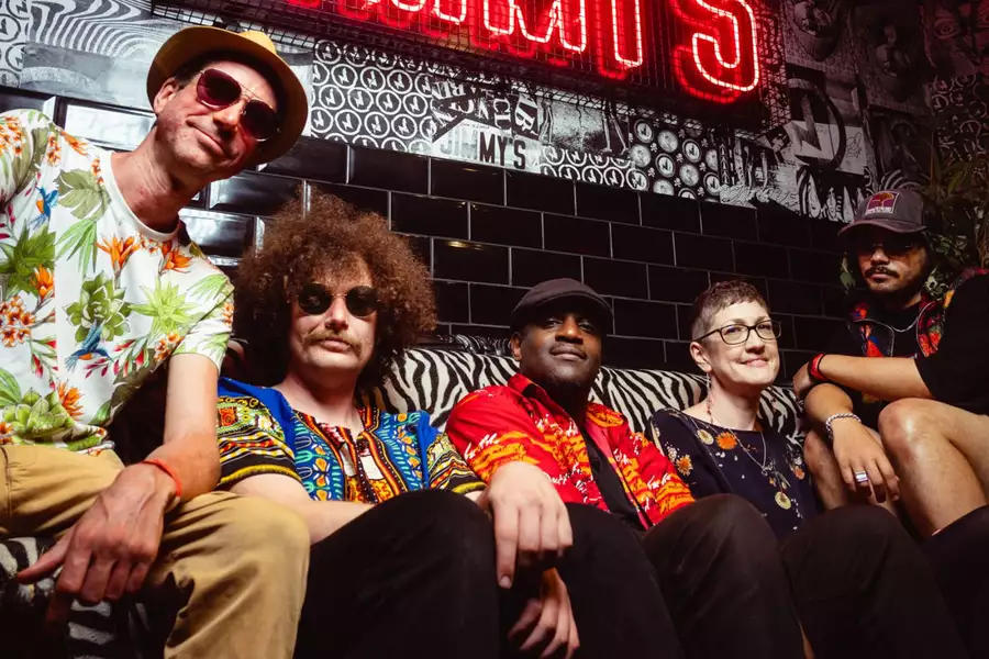 band NGUVU sit on a sofa in a bar smiling with a neon sign behind them