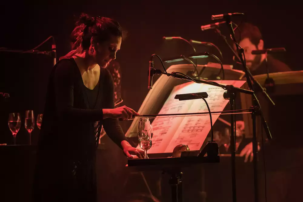 A member of Manchester Collective on stage using a violin bow to play music from water glasses