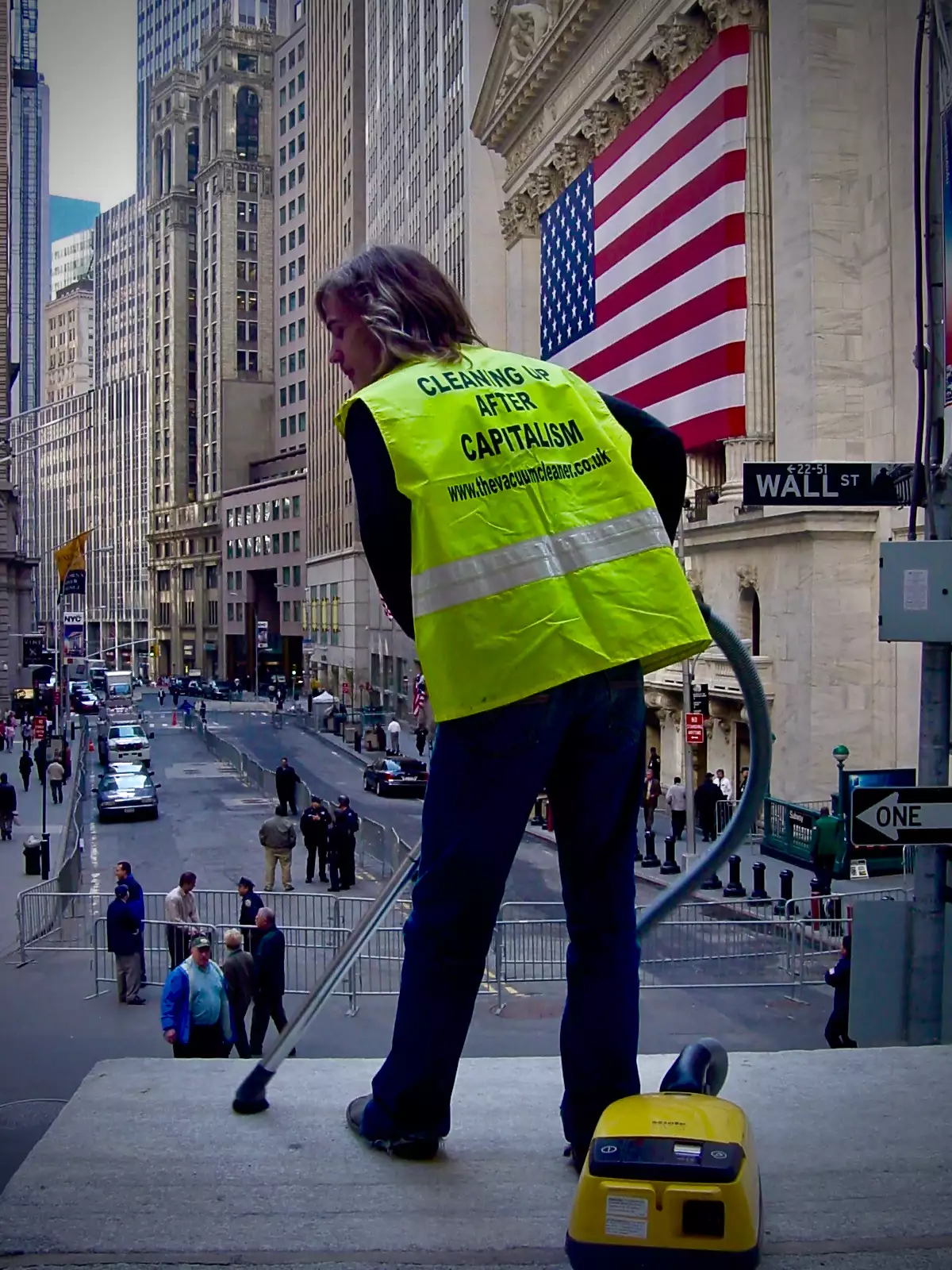 the vacuum cleaner using a hoover on Wall Street wearing a hi vis jacket