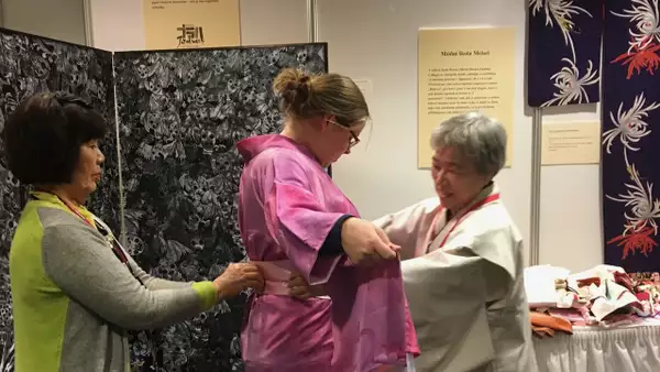 Two people helping someone dress in a kimono