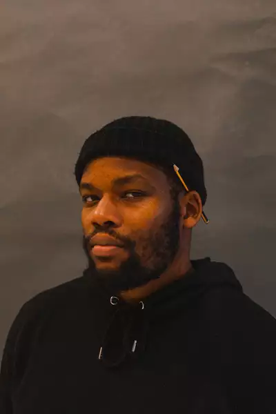 Headshot of Griot Gabriel, wearing all black with a pencil behind his ear