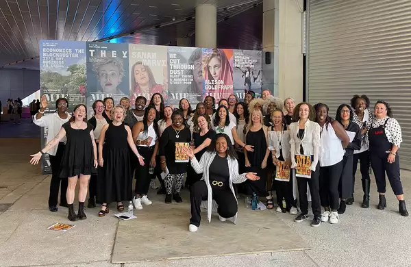 Group photo of NIA Choir, wearing black and white and smiling outside of Aviva Studios
