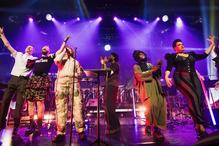 Multiple people on a stage singing, clapping and dancing with purple lighting