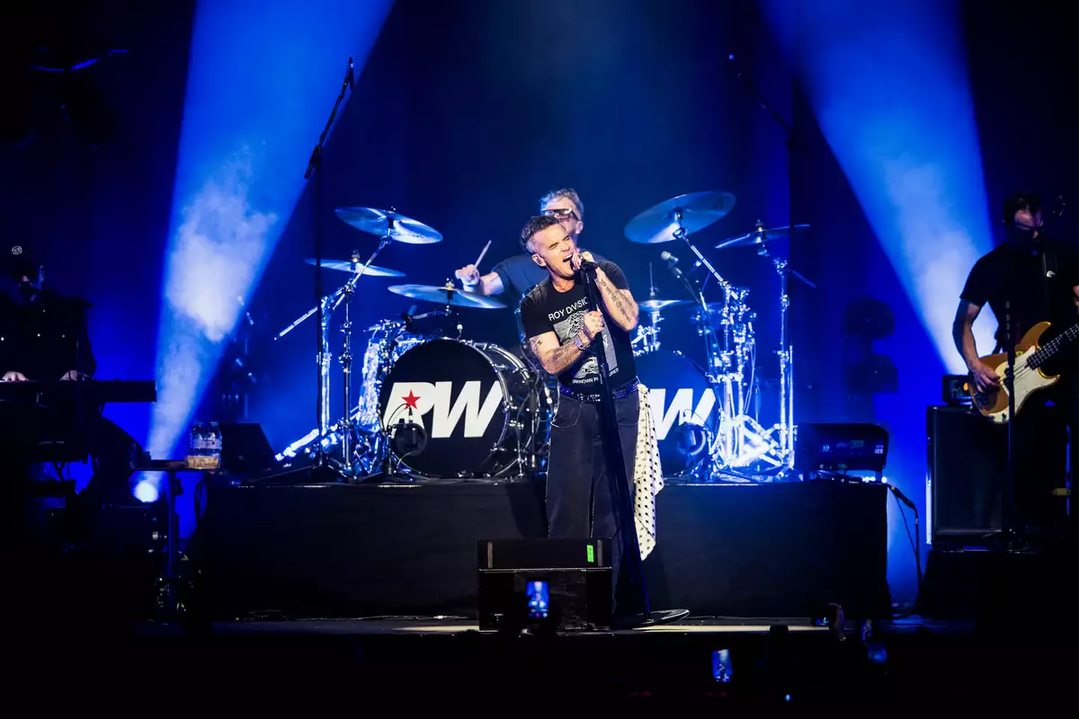 Robbie Williams on stage singing with blue lighting and his band