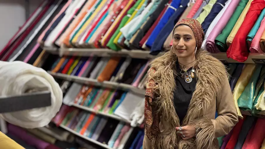 Zahra Nadeem wearing a fluffy brown coat, smiling in front of a shelf of fabrics