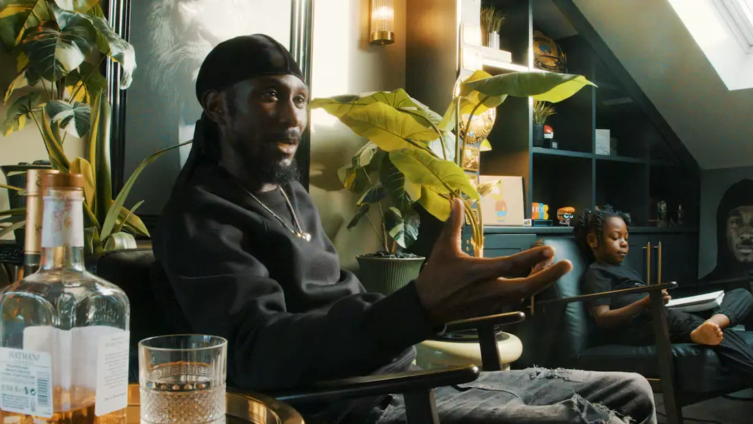 Cephas Williams sat on a chair talking surrounded by plants. His child is next to him.
