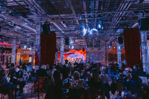 A crowd of people in the Social watching a performance on stage, with festive decorations around them