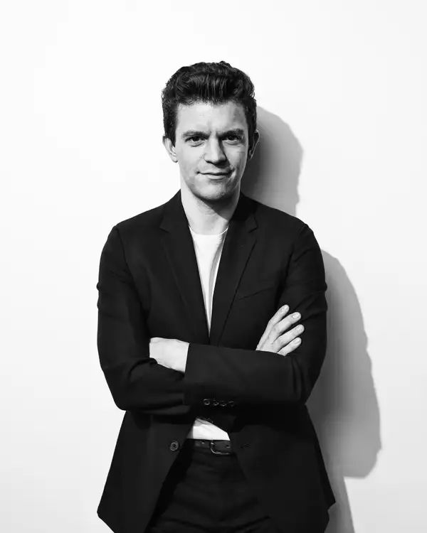 Black and white photograph of Tom Brady wearing a suit jacket with his arms crossed