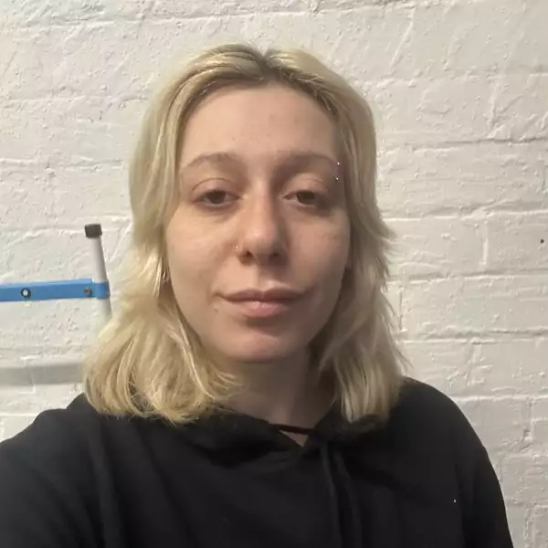 Square headshot of Madison Marcantonatos against a cream wall, wearing a black hooded jumper