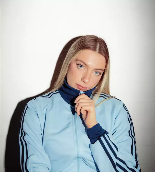 Photo of Amy Parton on a white background wearing a zipped up light blue Adidas tracksuit top