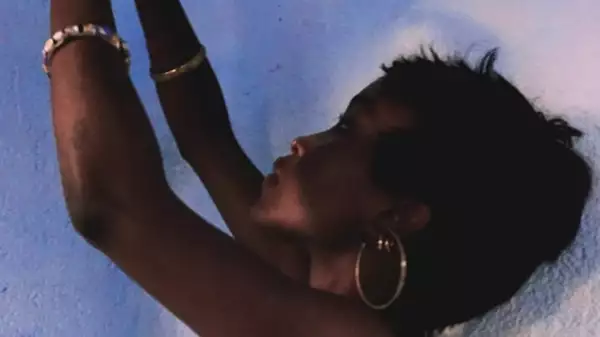 Softly blurred photo of Asandia holding her arms up against a light blue wall