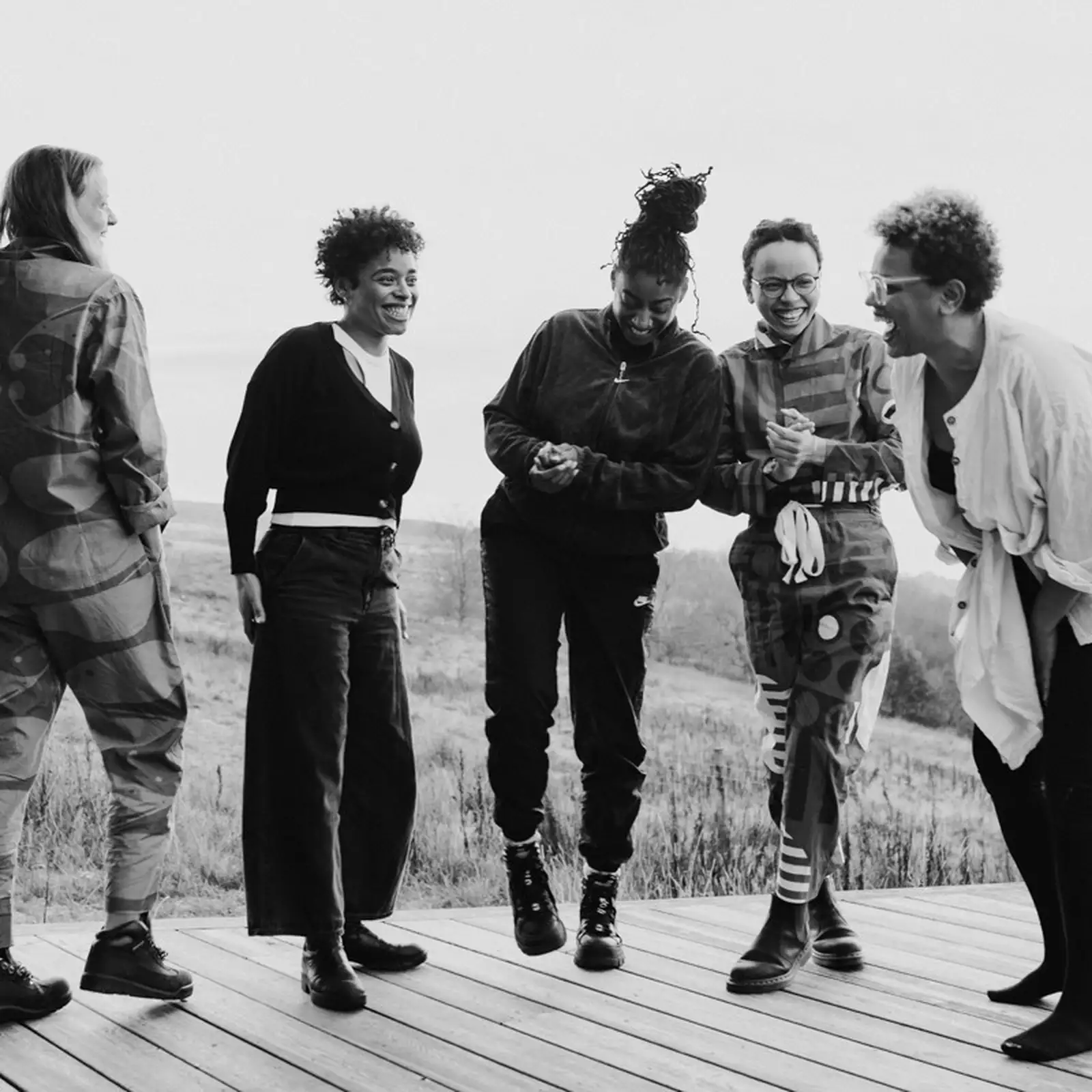 Black and white photograph of five people stood up laughing and smiling