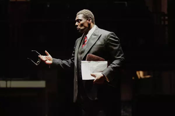 Photo of a man in a suit holding a briefcase pointing at something out of frame