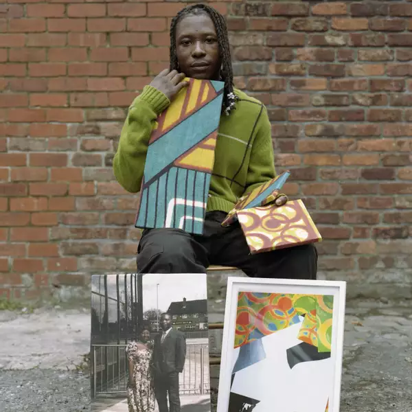 Photograph of Papa Nii Akushey Quaye sitting on a stool surrounded by his artworks