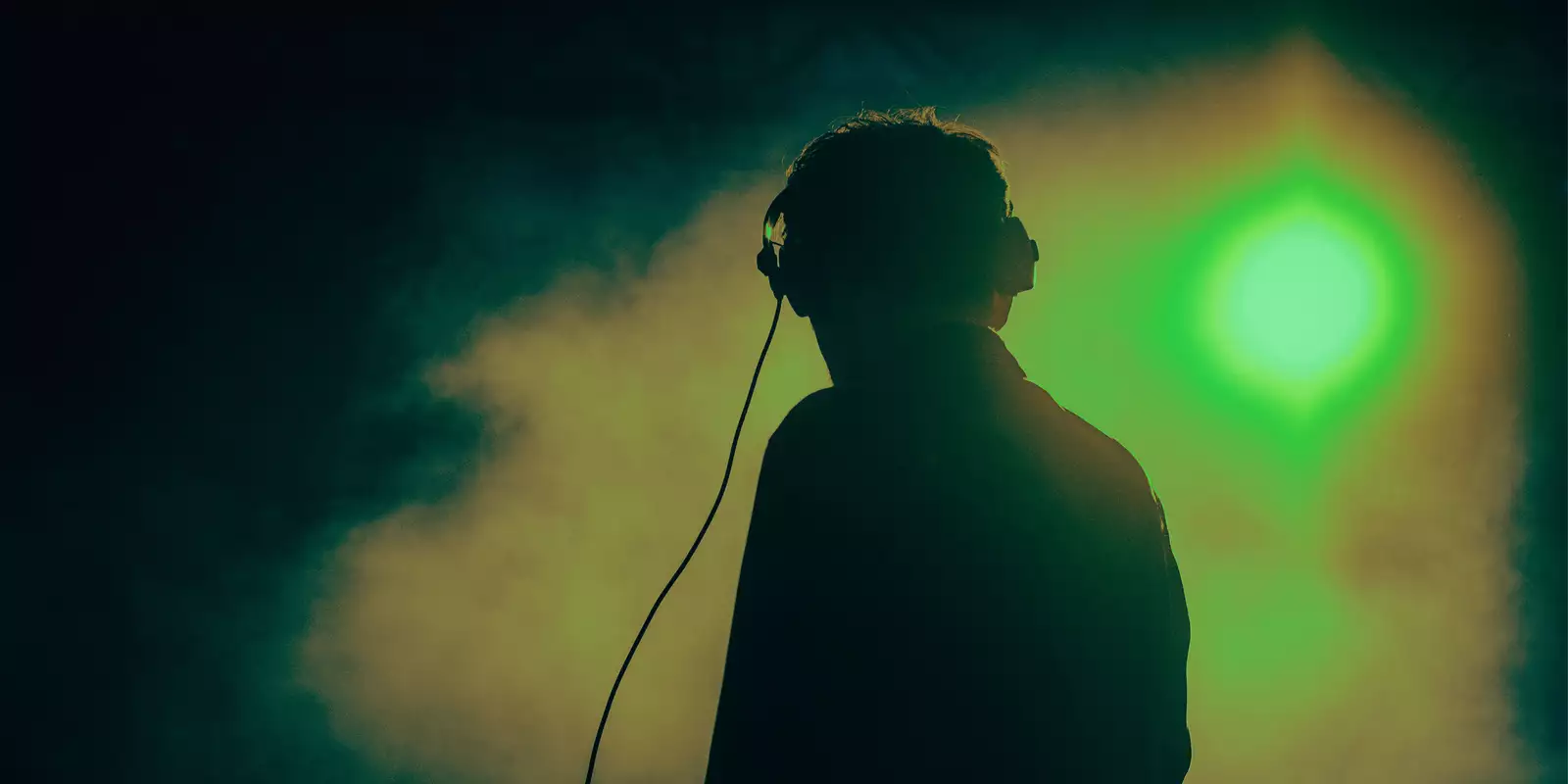 Musician on stage with headphones on with bright green lights