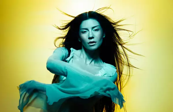 MARINA with long flowing hair poses against a yellow background