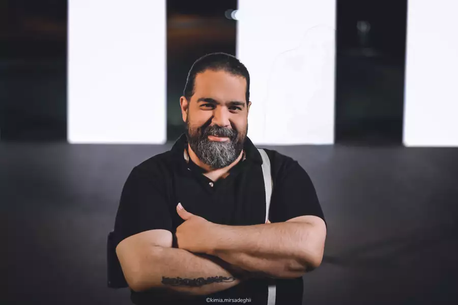 Reza Sadeghi in a black polo shirt smiling with his arms crossed.