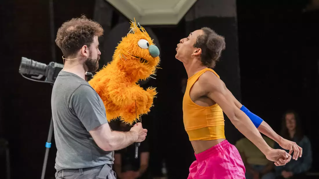 Two people on stage with an orange puppet performing