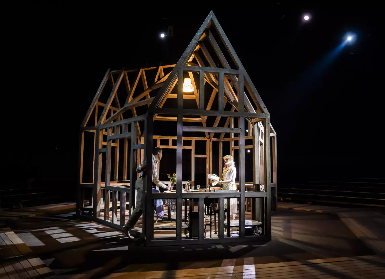 A structure of wooden beams in the shape of a house with a women standing in the middle