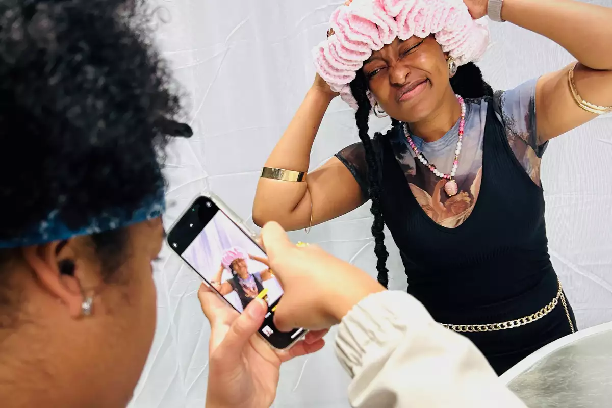 A person taking a picture on their phone of another person wearing a pink hat