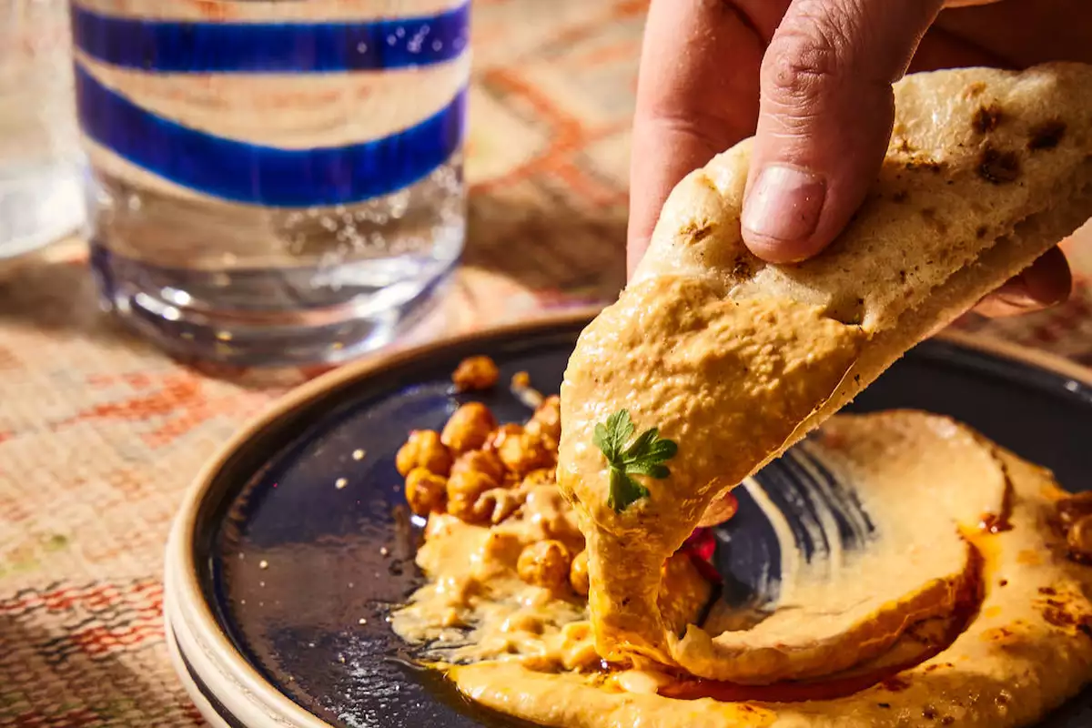 A hand dipping bread in hummus