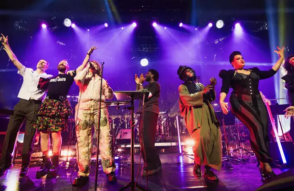 Multiple people on a stage singing, clapping and dancing with purple lighting