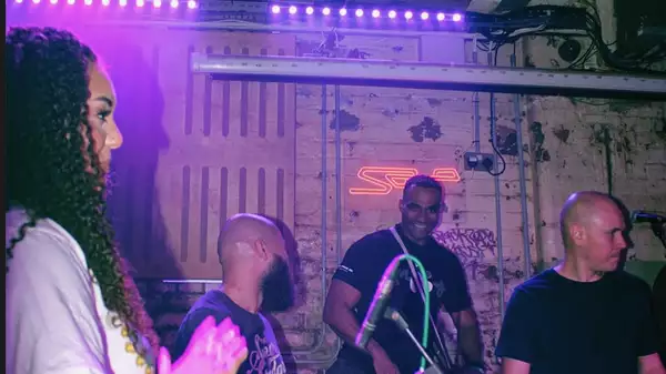 Four members of purple collective performing under purple lights