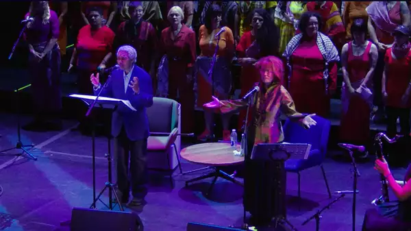 Beverley and Elizabeth Glenn-Copeland performing on stage with F* Choir wearing colourful clothes
