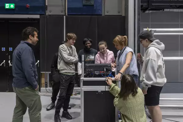 A group of people standing  around a mixing desk.