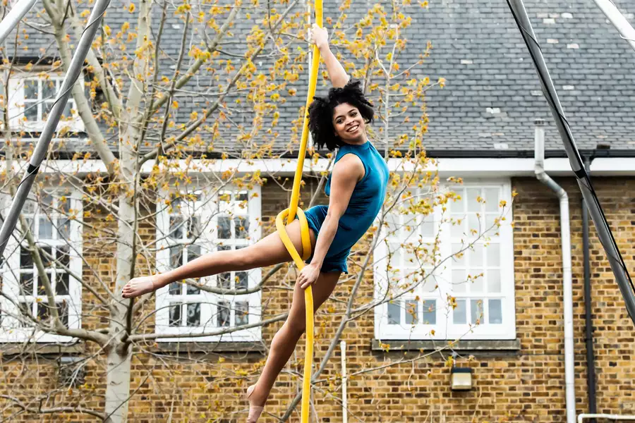 A dancer wearing a blue costume performing aerial rope dancing outside