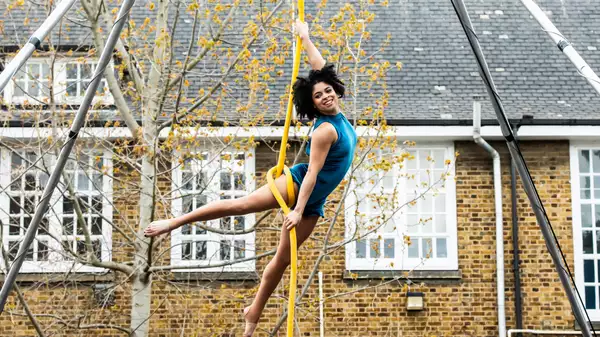 A dancer wearing a blue costume performing aerial rope dancing outside