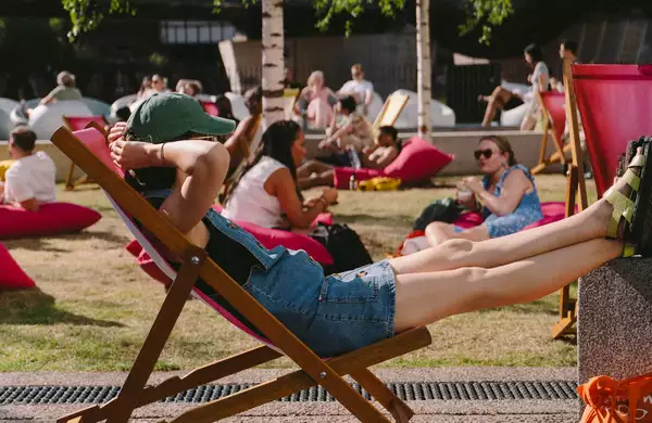 A person relaxing on a pink deck chair on grass outside Aviva Studios