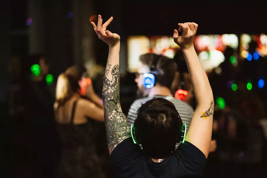 Photo of a person with their back turned, dancing with headphones in a crowd