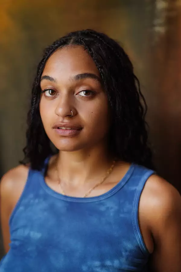 Pena Iiyambo in a tie-dye blue tank top against a brown background